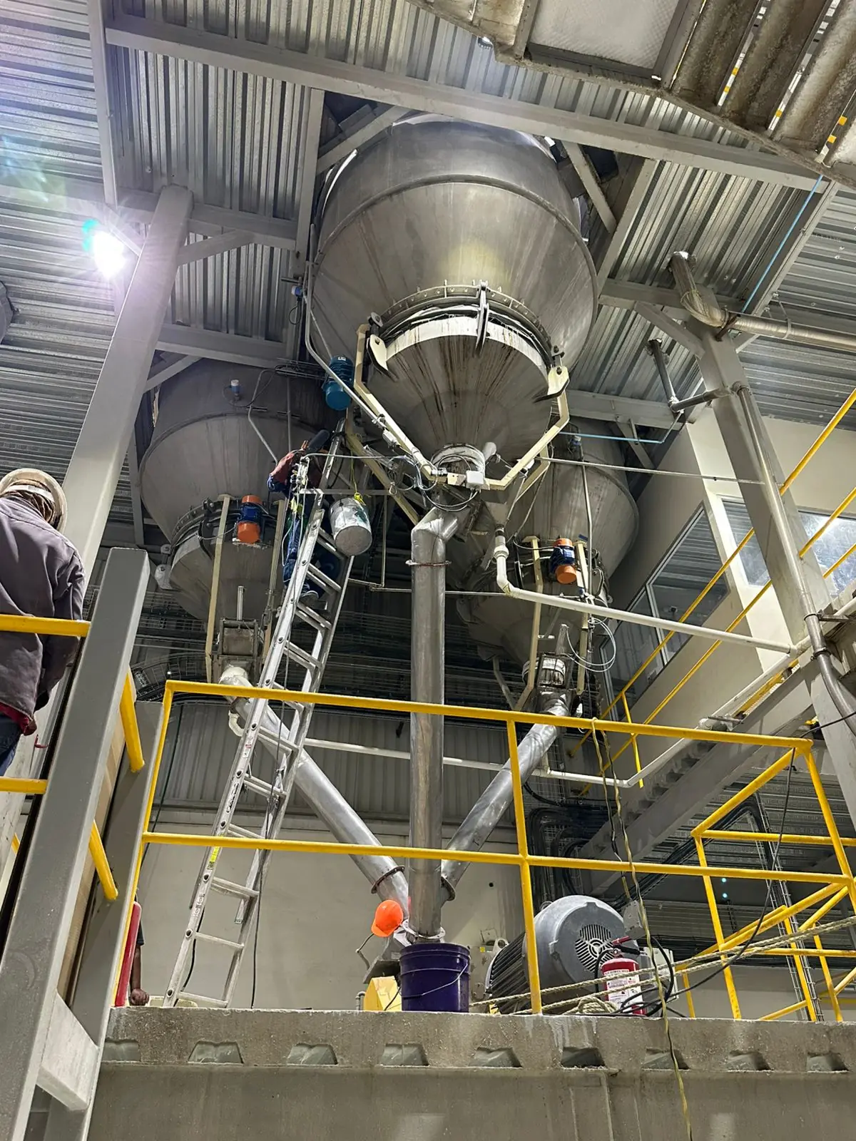 Técnico de Riker en escalera junto a una tolva en área de proceso